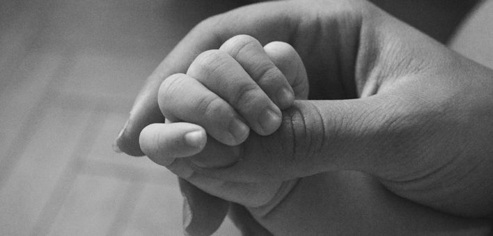Generic black and white photograph of an adult hand holding a baby's hand
