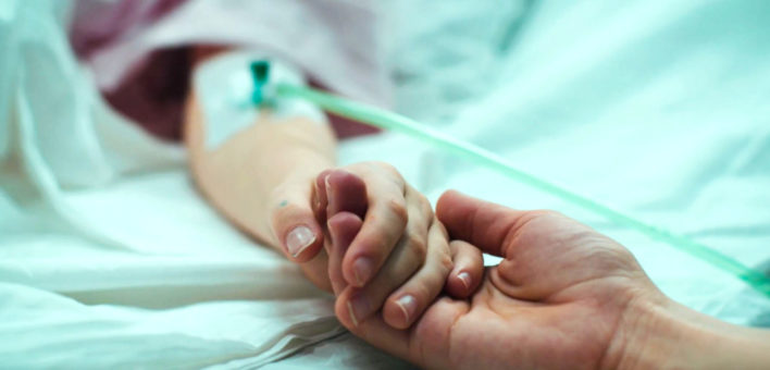 A hand gripping the hand of a hospital patient
