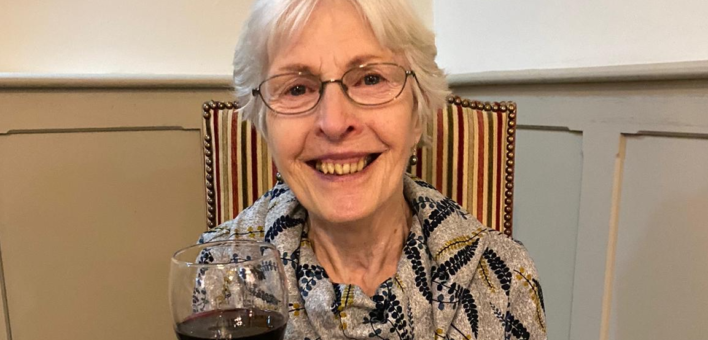 grey-haired woman holding glass of red wine smiling at camera