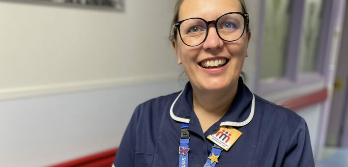 Nurse in hospital corridor smiling at camera