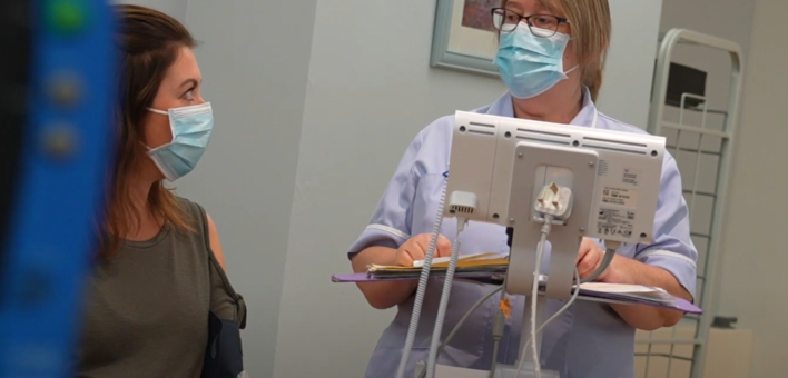 A patient wearing a mask talks to a nurse who is also wearing a mask.
