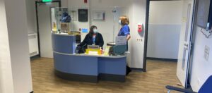 Reception desk at the eye clinic, a member of admin staff sits behind the desk, a nurse stands to her left.
