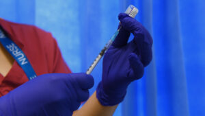 nurse preparing covid vaccine, she is wearing purple latex gloves