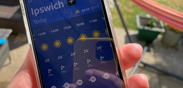 Mobile phone in foreground with weather showing sun and 24 degrees in ipswich